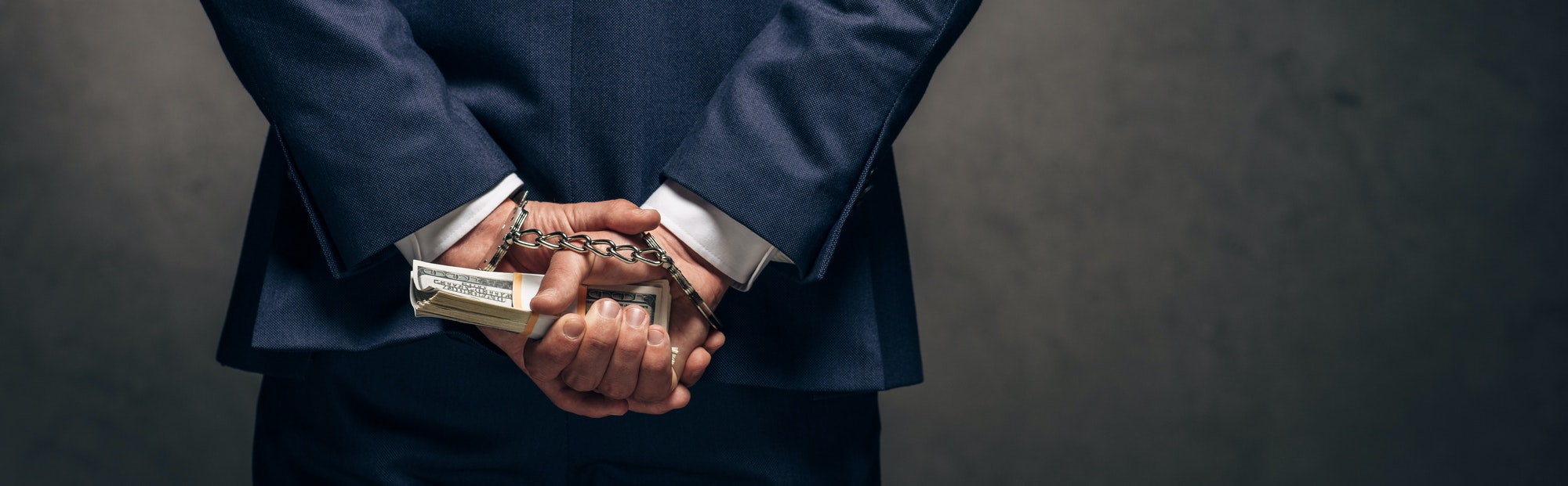 panoramic shot of handcuffed man holding bribe on grey